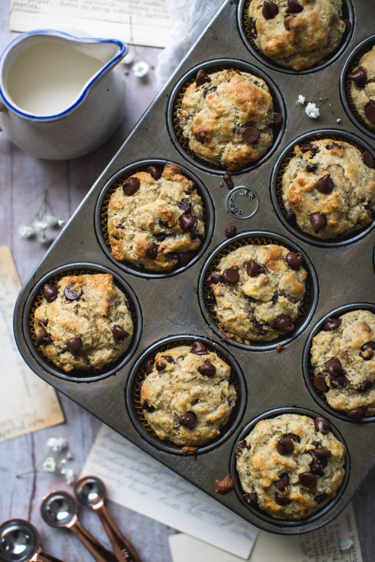 a muffin tin filled with chocolate chip muffins next to utensils