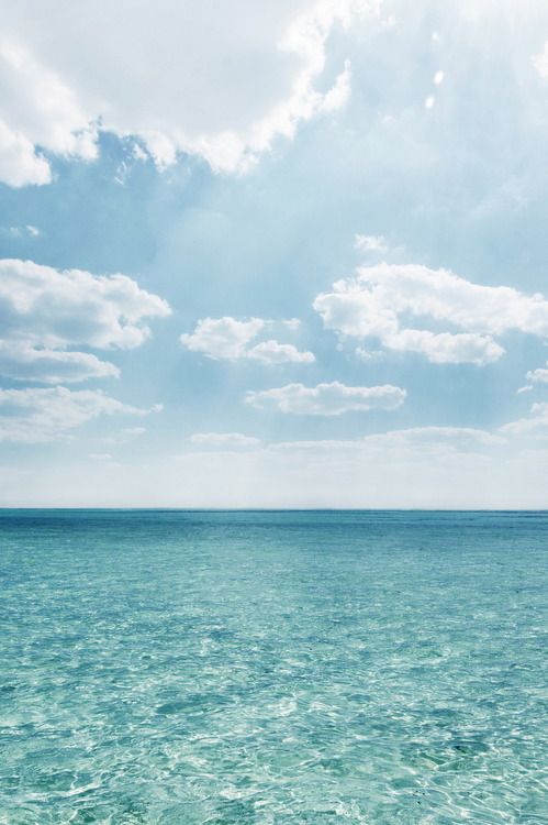 the ocean is blue and green with white clouds in the sky above it on a sunny day