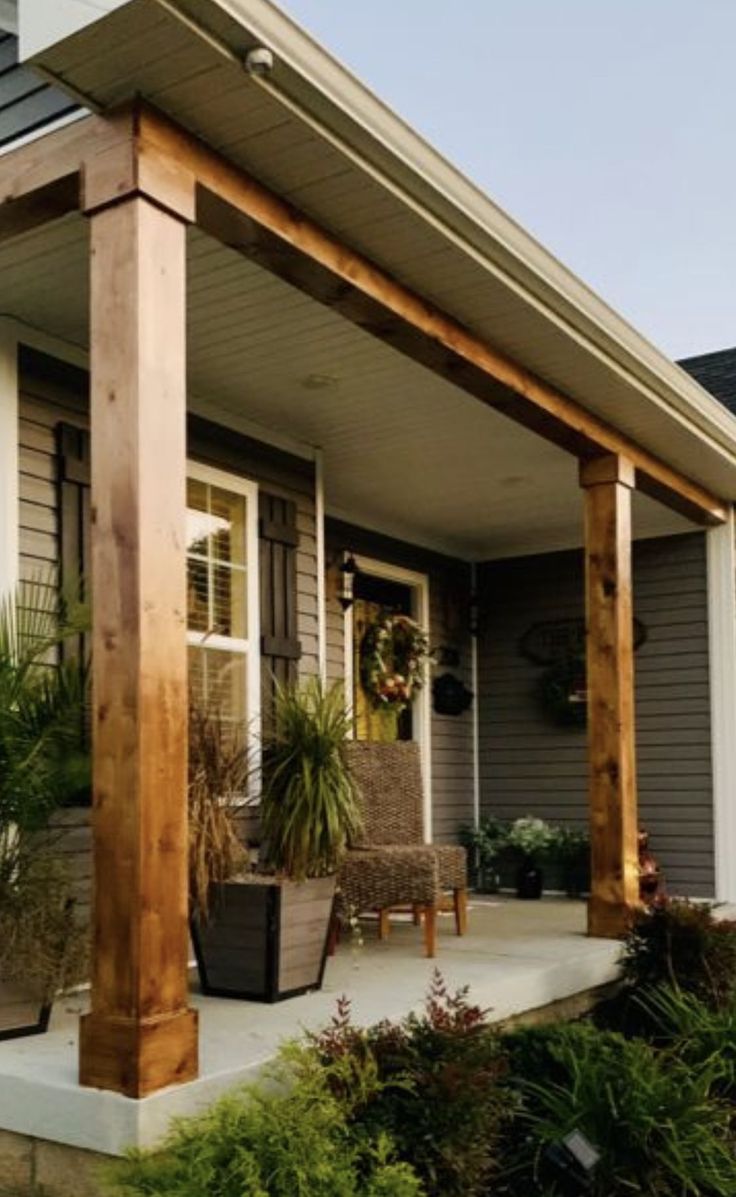 the front porch is covered with wooden posts and potted plants on the side walk