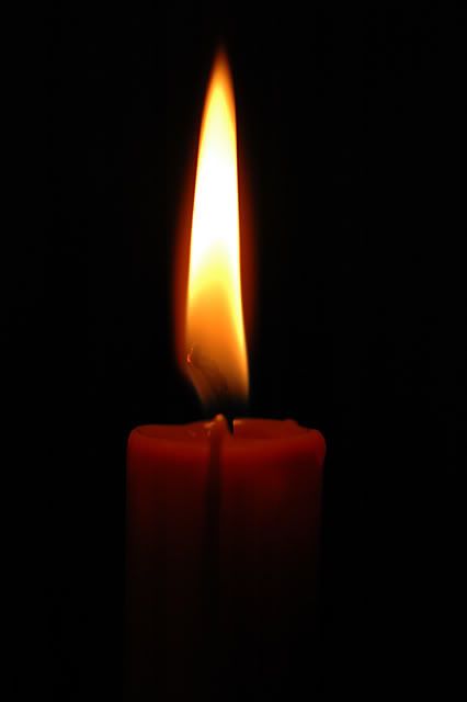 a lit candle in the dark with its bright flame glowing from it's center