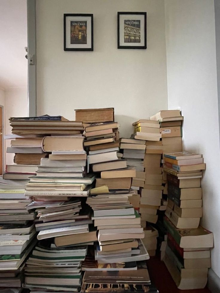 a pile of books sitting on top of a wooden floor next to a wall filled with pictures