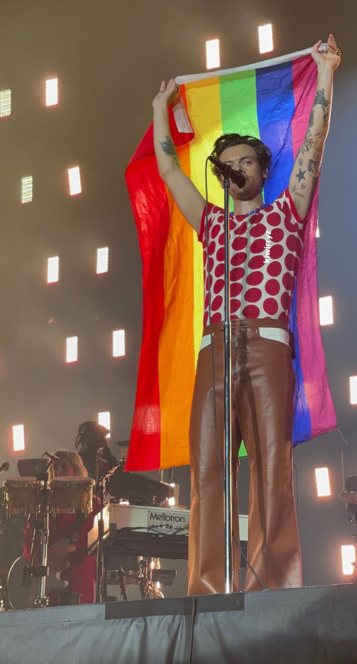 a man holding a rainbow flag while standing in front of a stage with his hands up