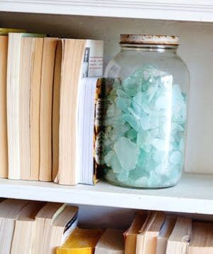 a glass jar filled with green rocks sitting on top of a shelf next to books