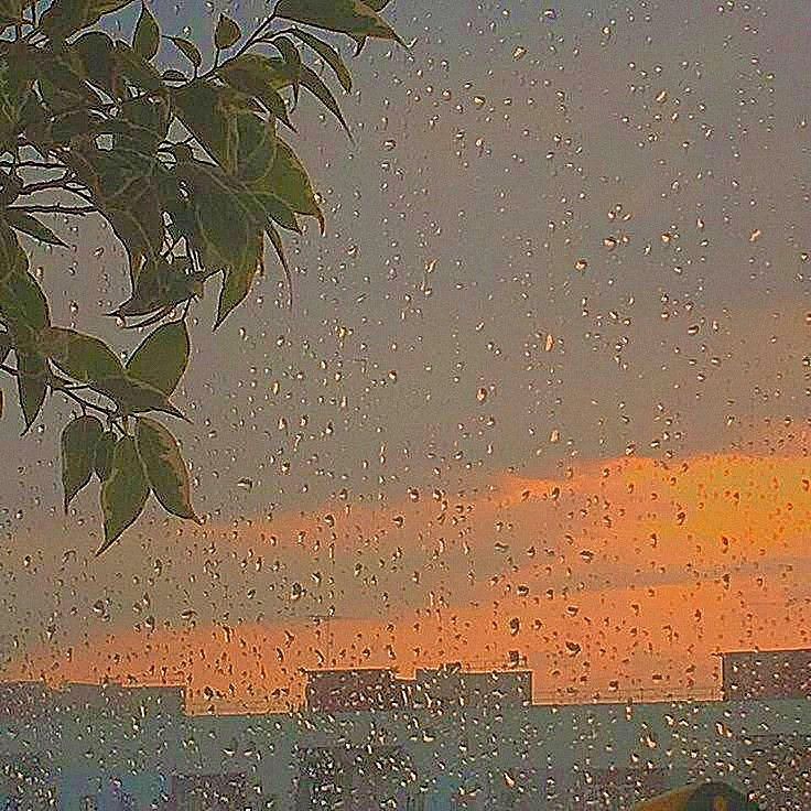 the sun is setting behind some buildings and raindrops on a window pane