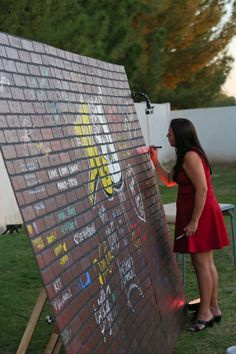 a woman in a red dress is writing on a brick wall with marker markers and an easel