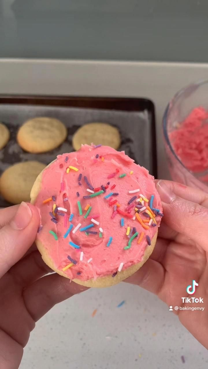 a person holding a pink frosted doughnut with sprinkles