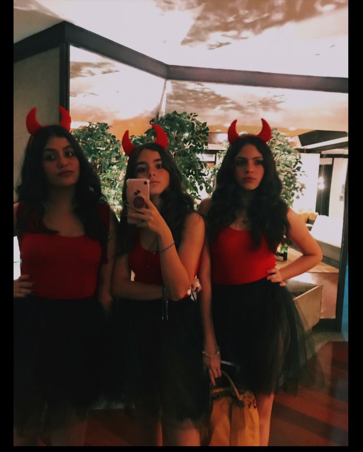 three women dressed up in devil costumes taking a selfie with their cell phone while standing next to each other