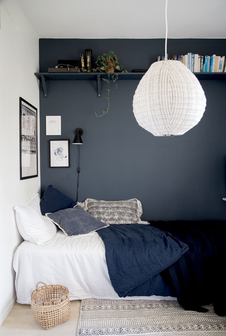 a bedroom with a bed, bookshelf and hanging lamp in the corner next to it