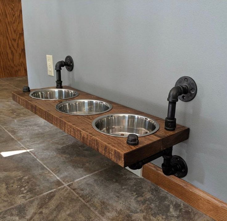 three stainless steel bowls sit on a wooden shelf in the middle of a tile floor