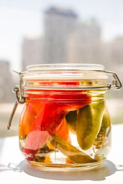 a jar filled with pickles sitting on top of a table next to a window