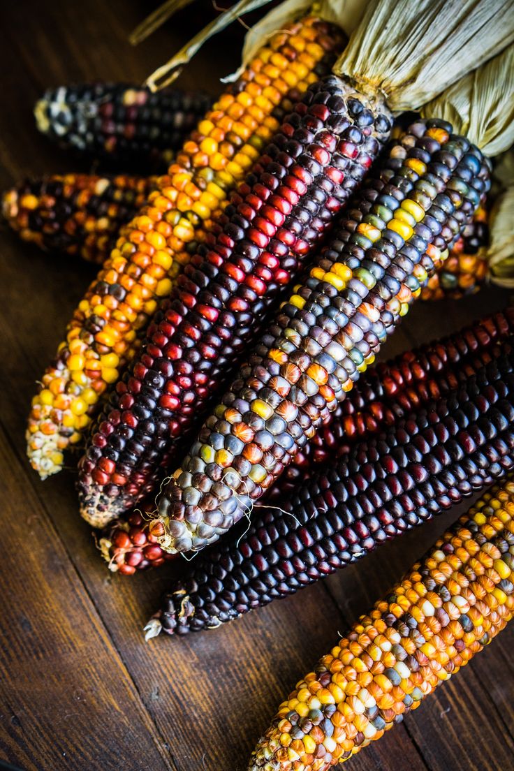 corn on the cob is sitting on a wooden table with other vegetables in it