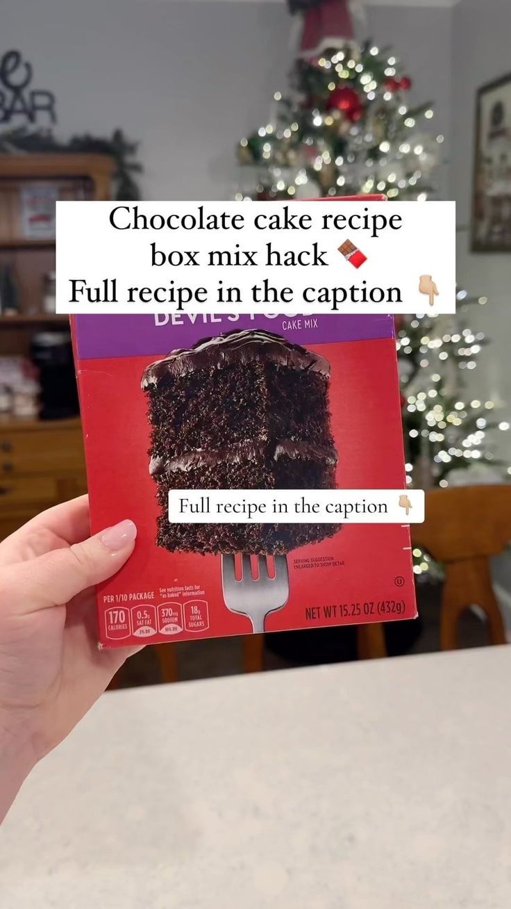 someone holding up a box of chocolate cake with the recipe on it, in front of a christmas tree