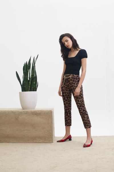 a woman standing next to a potted plant wearing leopard print pants and red shoes