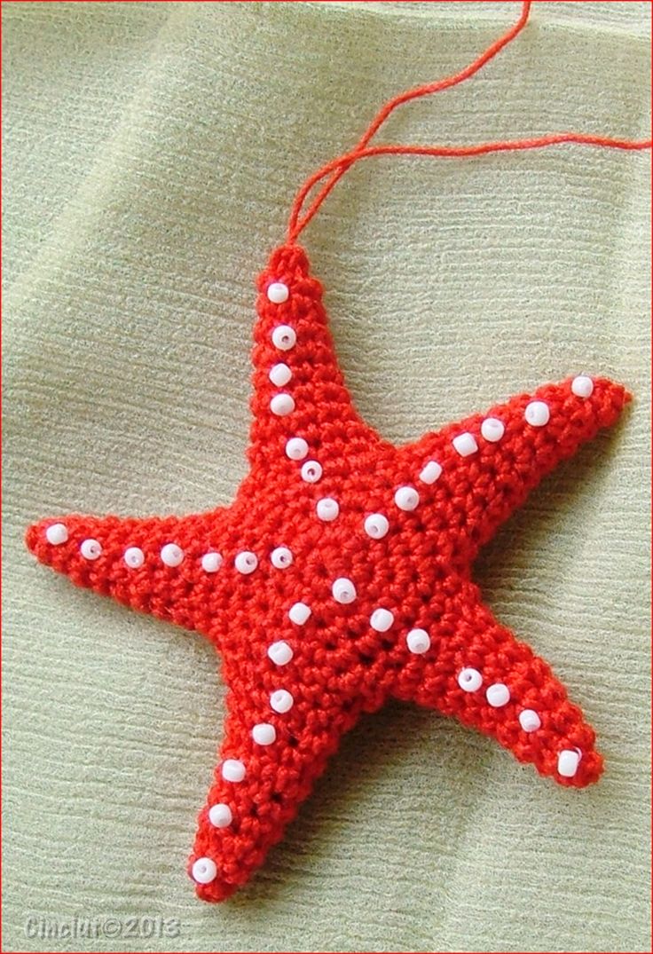 a red crocheted starfish ornament hanging on a white cloth background