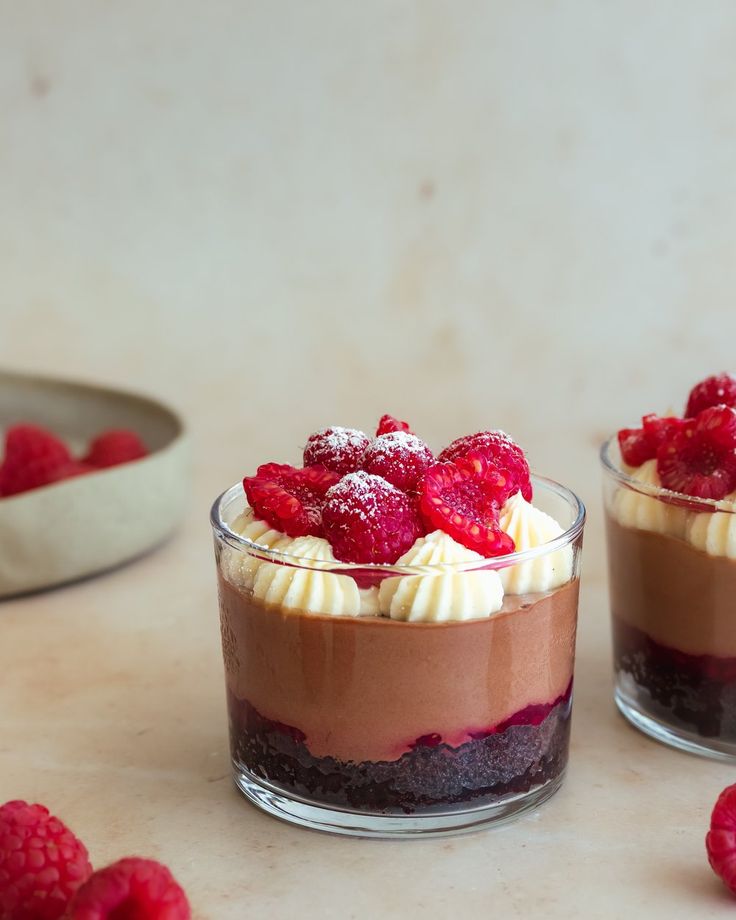 two desserts with raspberries and whipped cream on top are sitting on a table