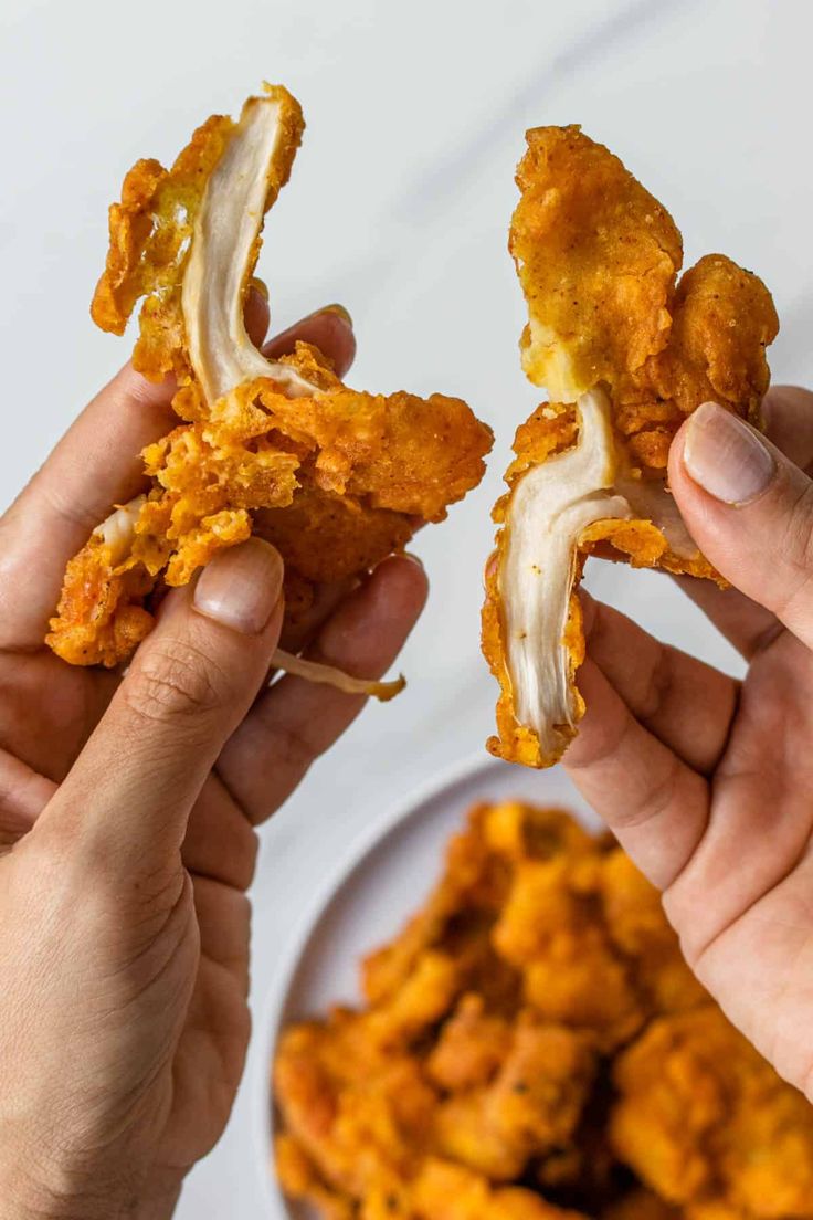 two hands holding up pieces of fried chicken