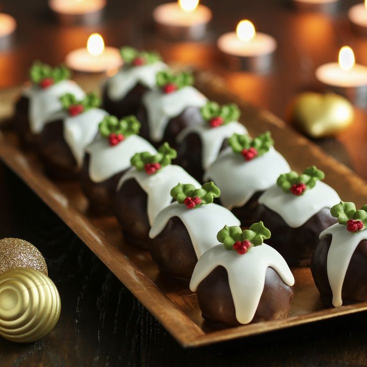 chocolate covered pastries with white frosting and holly decorations on a wooden platter