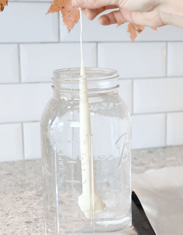 a person is pouring white liquid into a glass jar with leaves on the counter top