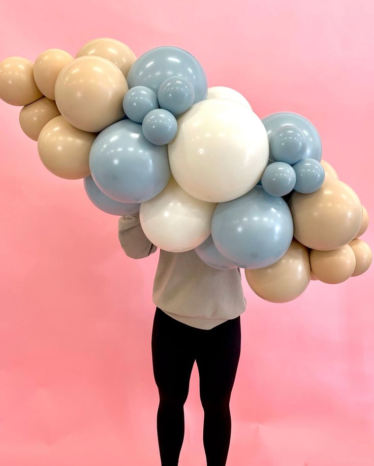 a person holding balloons in the shape of a cloud on a pink background with black pants