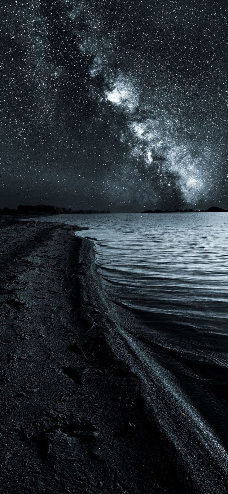 the night sky is filled with stars above water and sand on the beach, as well as an ocean shore