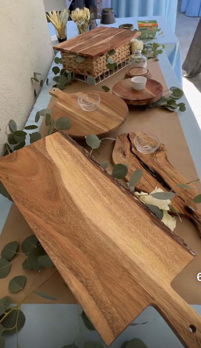 wooden cutting boards sitting on top of a table covered in leaves and greenery next to baskets