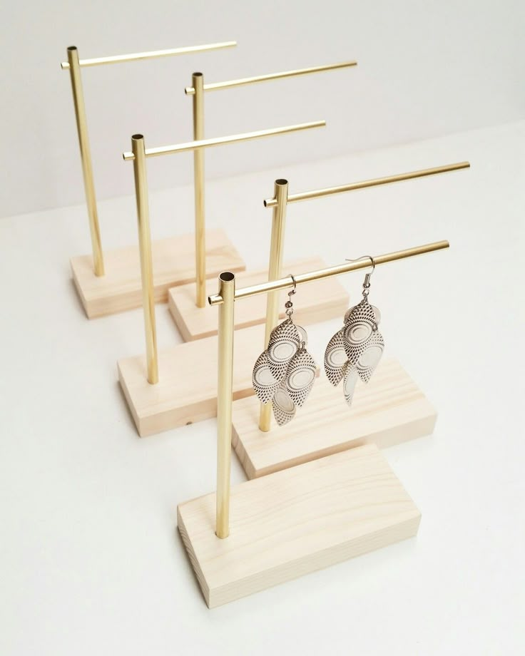 three pairs of earrings are displayed on wooden stands with metal bars and hooks for earring holders