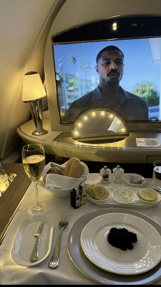 a man is on the screen in an airplane with food, wine glasses and silverware