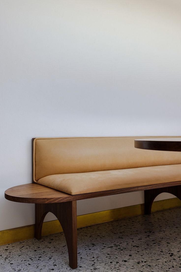 a wooden bench sitting on top of a floor next to a white wall and yellow trim