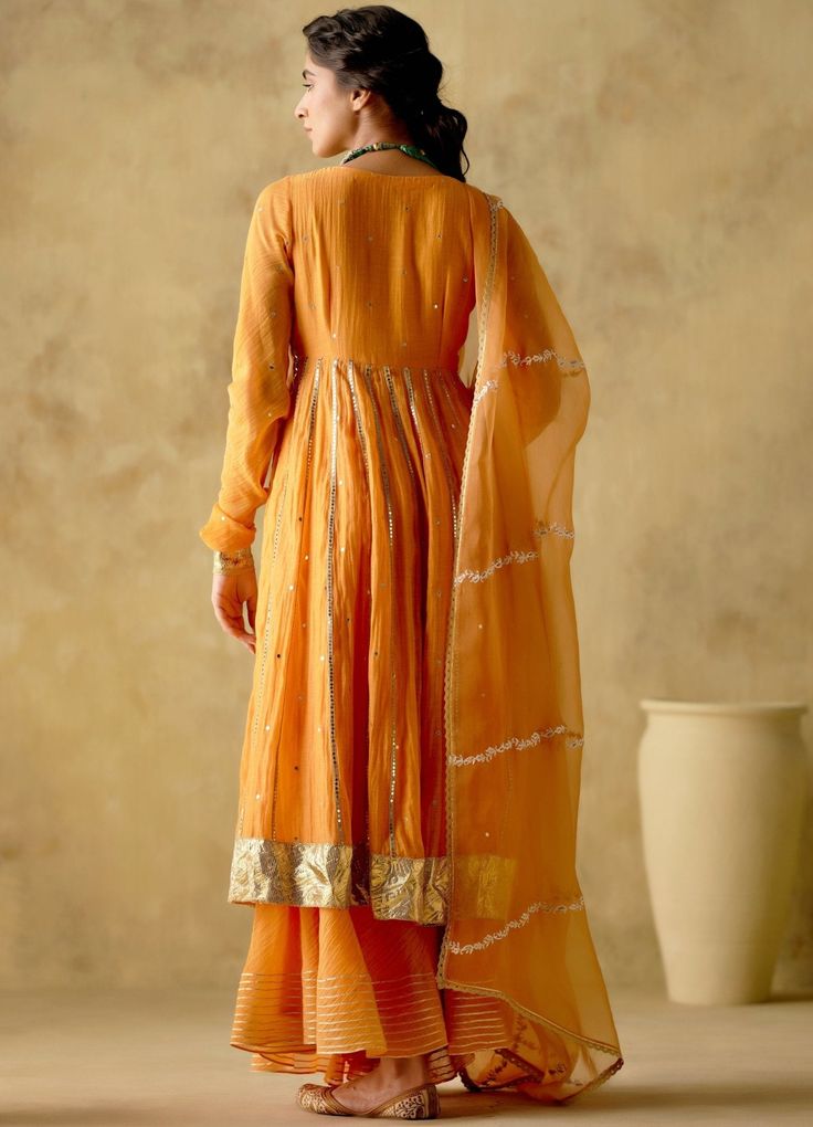 Features a tangerine front open silk anarkali embellished with zari & patra work, finished with gota lace & button detailing on the front. Completed with a matching sharara with lace detailing and an embellished dupatta. Composition : Anarkali & Sharara: Chanderi Silk Lined with Mul Cotton, Dupatta: Organza Care: Dry Clean Only and Vacuum Storage All products can be customised for sleeves, length of blouse and neck design Delivery : 3-4 weeks as the product is hand crafted. Check Size Guide or choose MySize for free customisation (All Sizes above XL can be made at 15% additional cost) For more information and sizes please contact fabiliciousfashion@gmail.com or visit our Copenhagen studio. Orange Anarkali, Silk Anarkali, Embroidered Anarkali, Indian Wedding Wear, Cotton Dupatta, Lace Button, Embroidered Dupatta, Sharara Set, Lace Embroidery