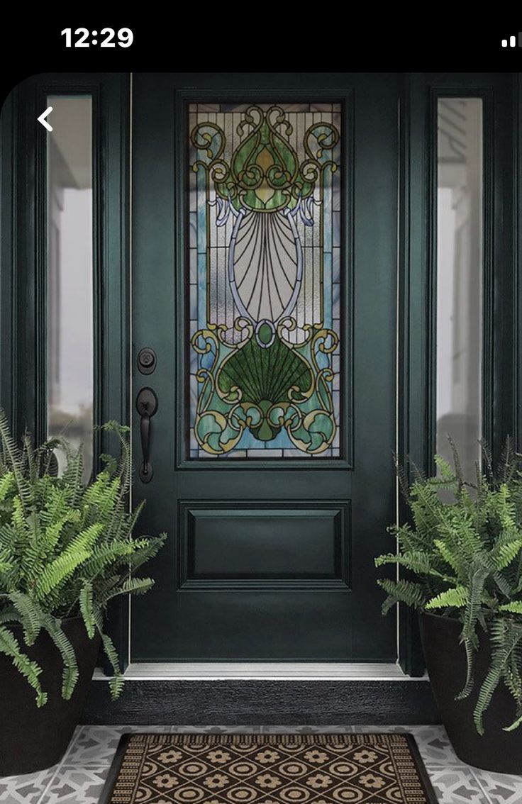 a green front door with stained glass and potted plants