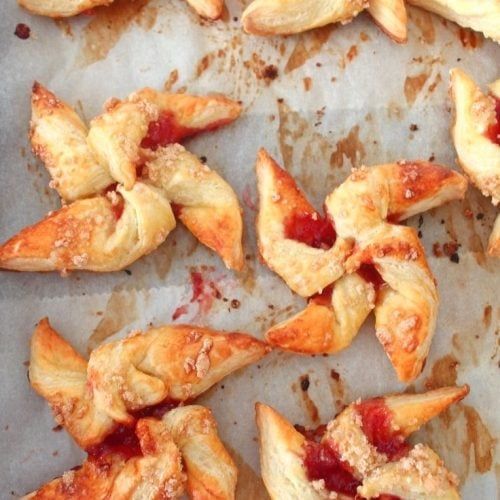 several pastries on a baking sheet with cranberry sauce and almonds in the background