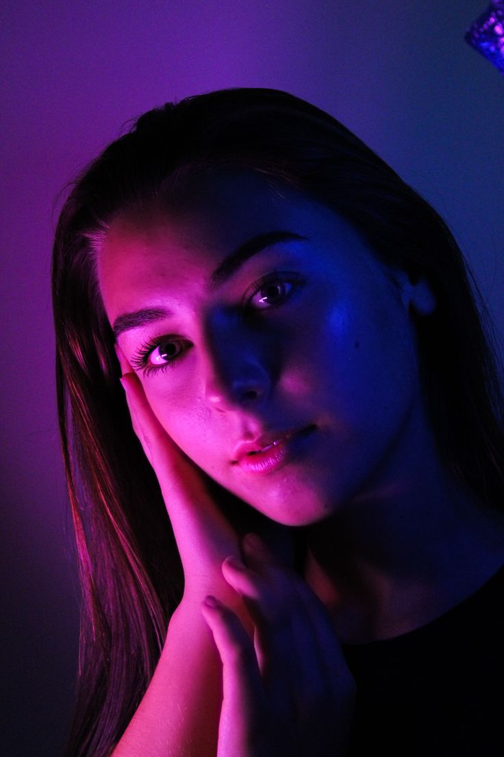 a woman with her hand on her chin looking at the camera while standing in front of a purple light