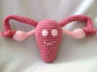 a pink crocheted object with eyes and arms