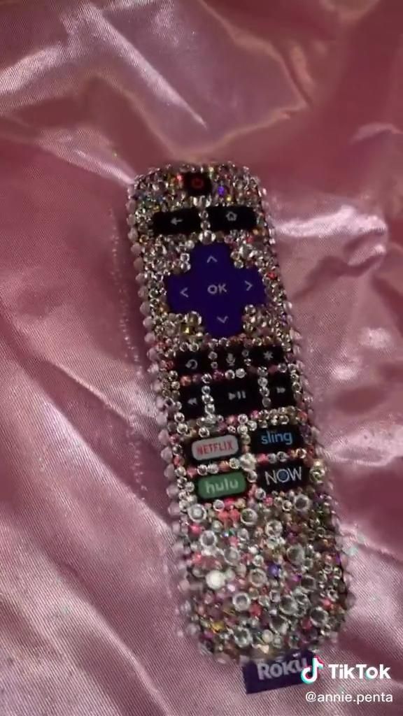 a cell phone covered in lots of different types of jewels on a pink satin surface