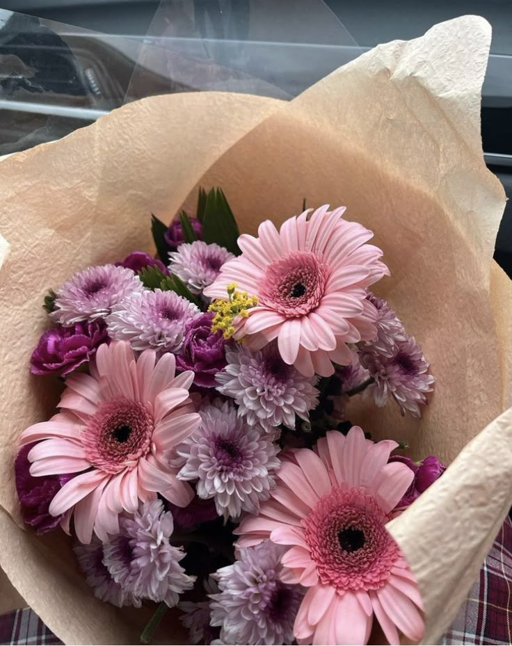 a bouquet of pink and purple flowers sitting on top of a plaid cloth covered table