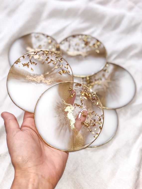 a hand is holding four glass coasters with gold sprinkles