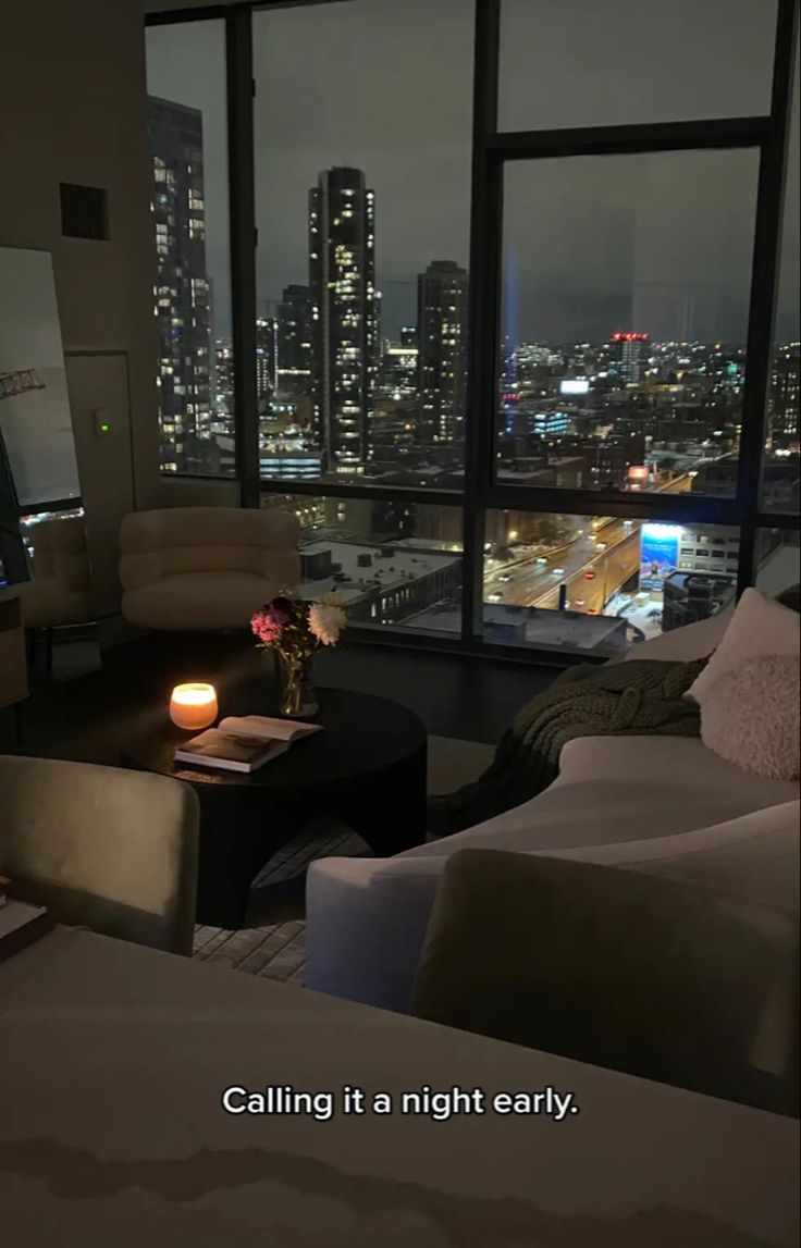 a living room filled with furniture and a large window overlooking the city at night time