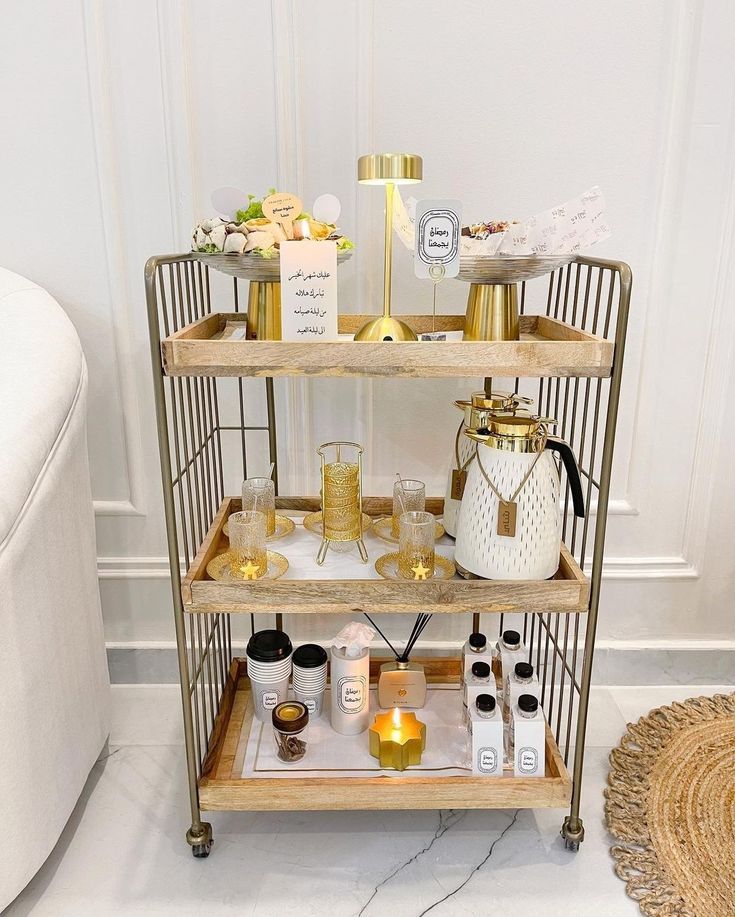 a three - tiered bar cart with bottles and glasses on it in front of a white wall