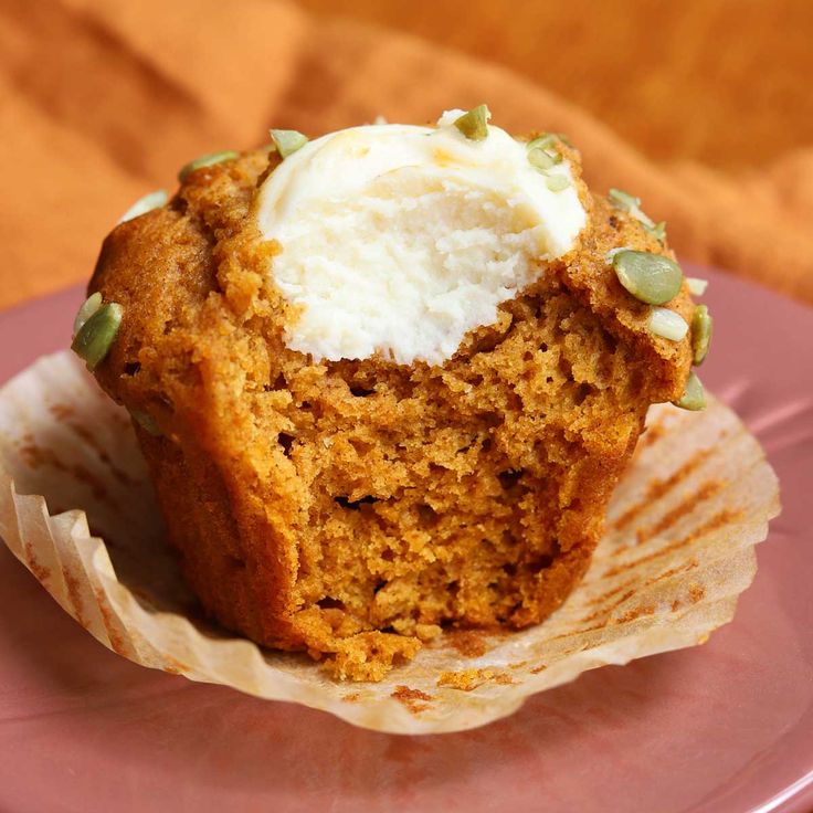 a muffin on a pink plate topped with whipped cream and pistachio seeds