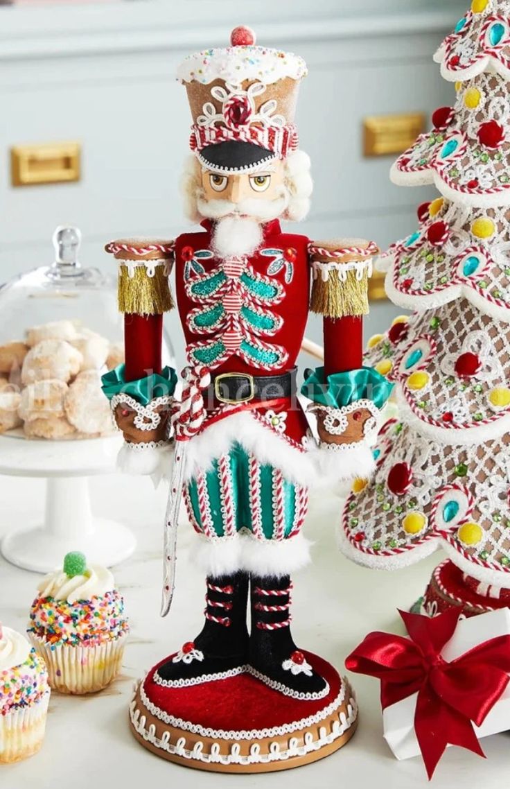 a nutcracker figurine next to a christmas tree and cupcakes