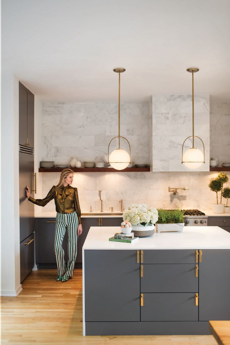 a woman standing in the middle of a kitchen with marble counter tops and gray cabinets