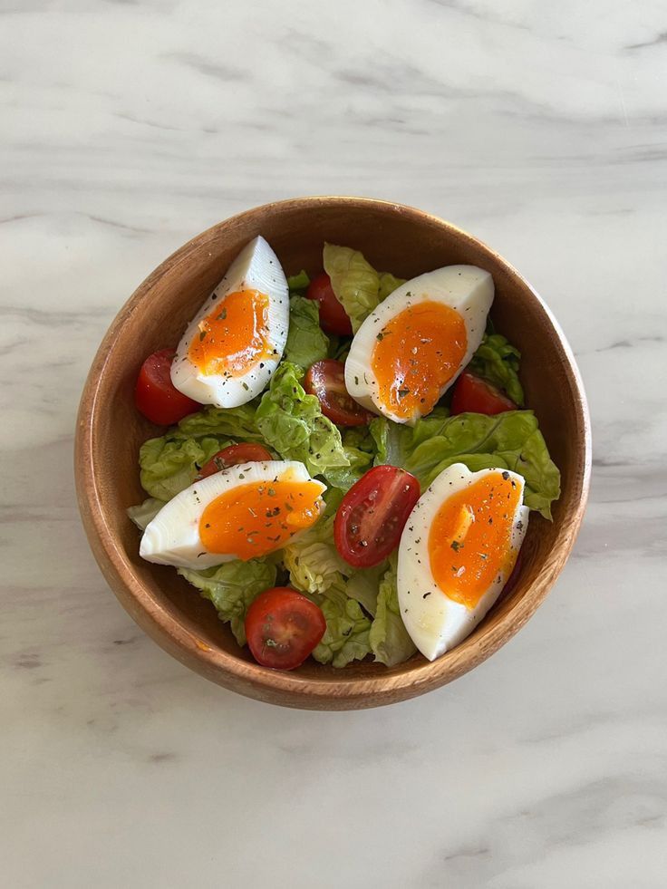 a wooden bowl filled with lettuce and hard boiled eggs on top of tomatoes