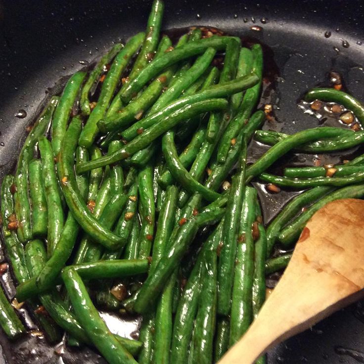 green beans are being cooked in a wok with a wooden spoon on the side