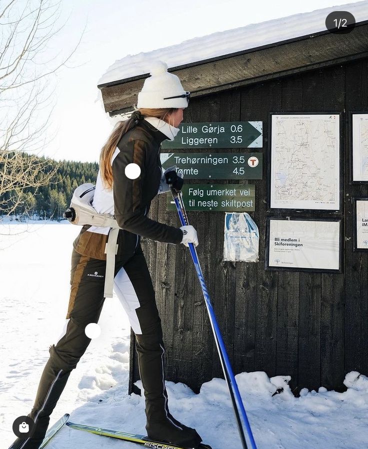 a woman on skis standing in front of a wooden building with snow and signs