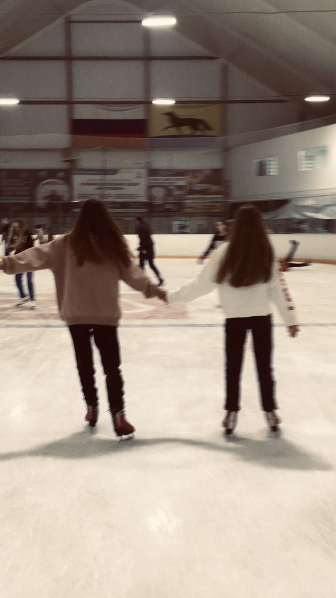 two girls are holding hands while skating on an ice rink with other people in the background