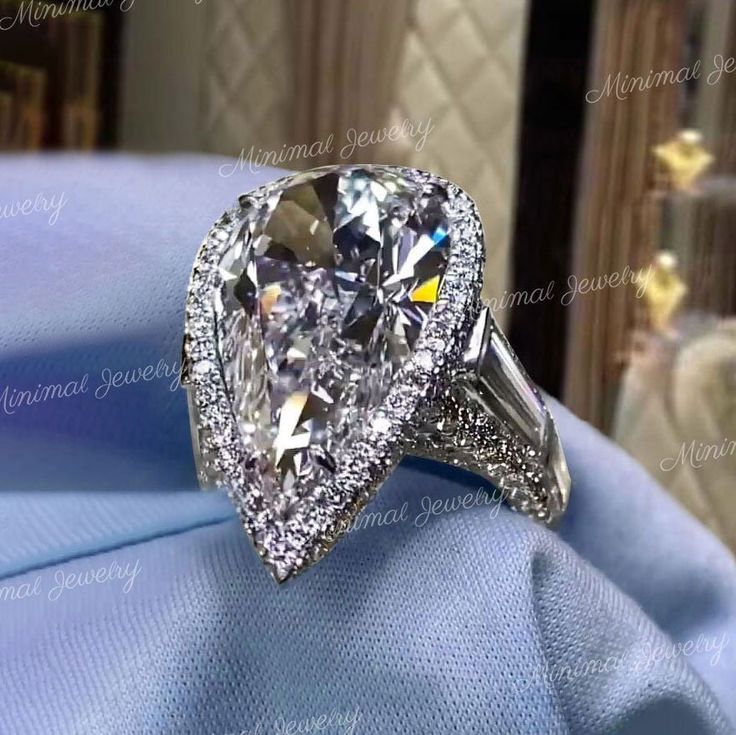 an engagement ring with a pear shaped diamond in the center on a blue satin cloth