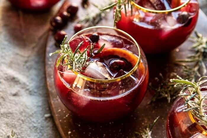 two glasses filled with red liquid and garnished with herbs on a cutting board