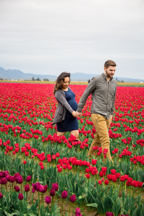 a pregnant couple walking through a field of tulips