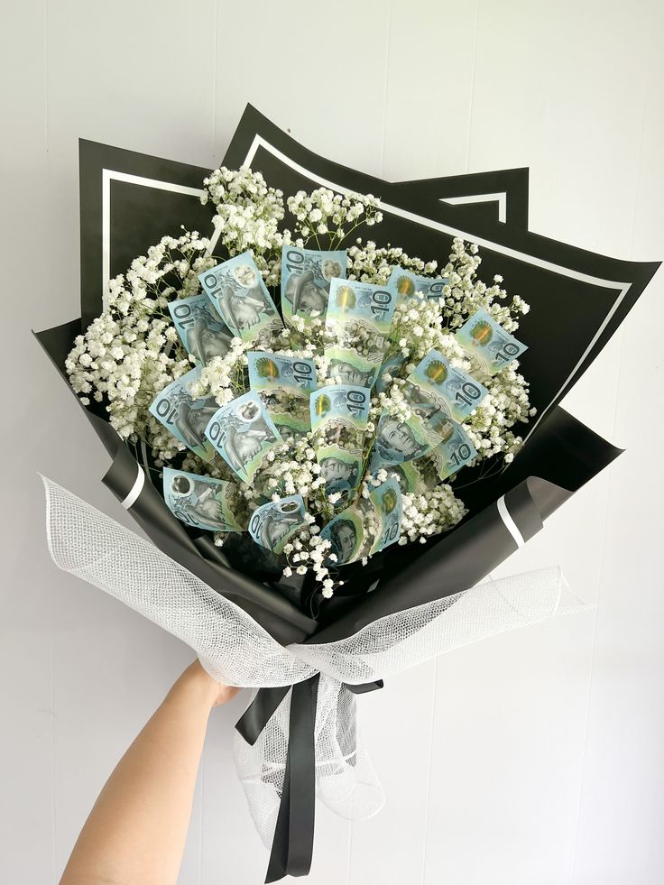 a bouquet of flowers is wrapped in black paper and tied to a white ribbon with money notes on it