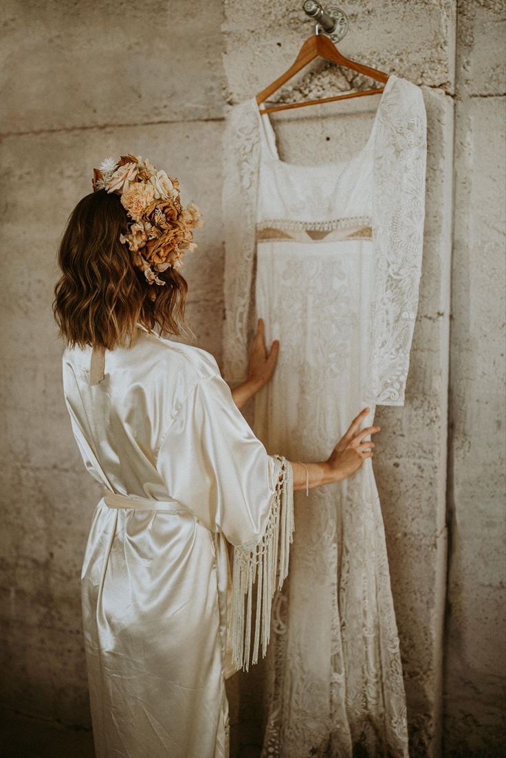 a woman standing next to a dress on a hanger in front of a wall